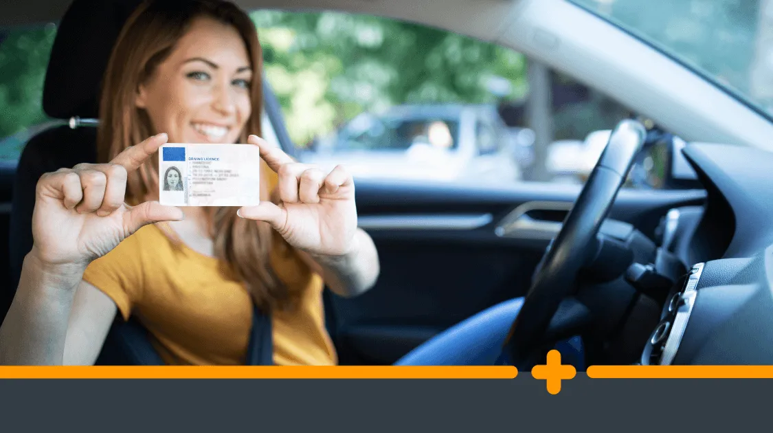Uśmiechnięta młoda kobieta siedząca w samochodzie, trzymająca w dłoniach prawo jazdy i prezentująca je do kamery.
